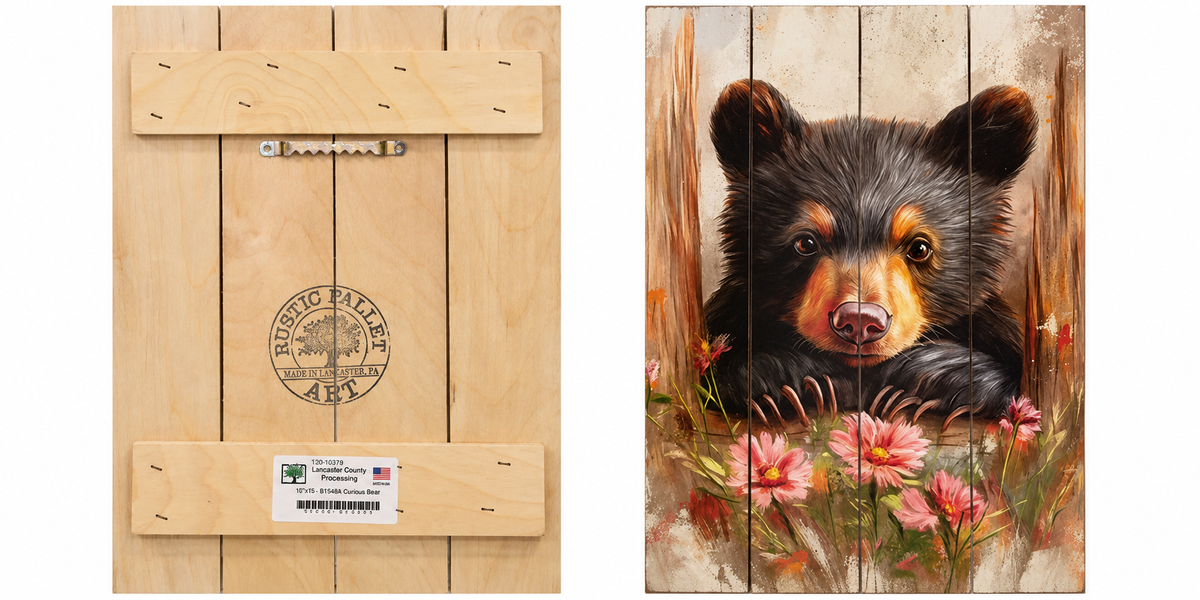 A rustic wooden wall art piece shown front and back. The front features a painted black bear cub peeking through pink flowers against a weathered wood background.