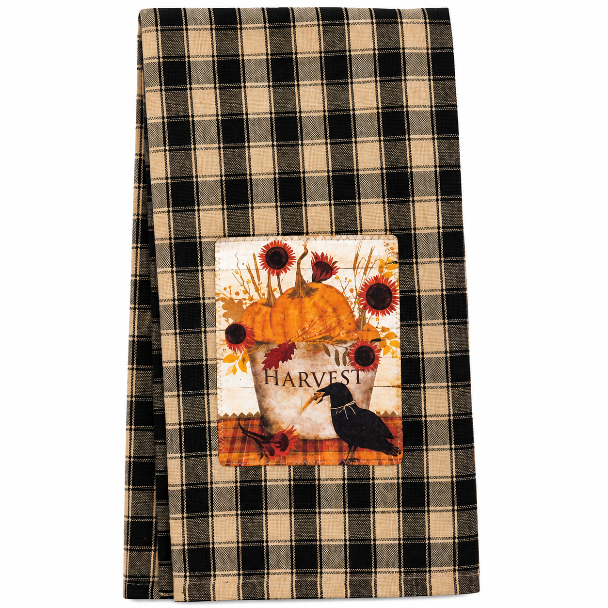 A folded kitchen towel with a black and beige plaid pattern, featuring a central autumn-themed patch with a pumpkin, sunflowers, leaves, and a crow above the word 'HARVEST'.