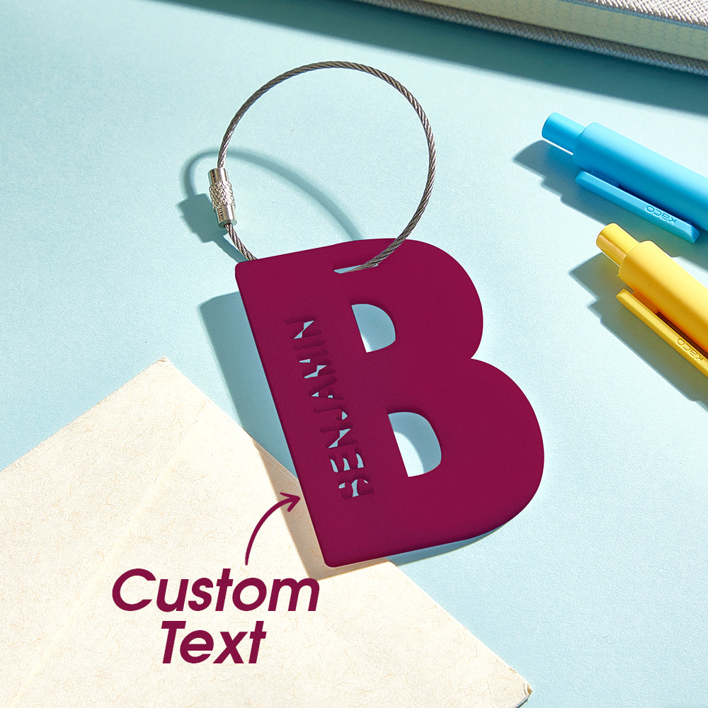 A close-up view of a 3D printed luggage tag featuring the letter "b" in wine red, with a text overlay that says "Custom text" to highlight the personalization option.