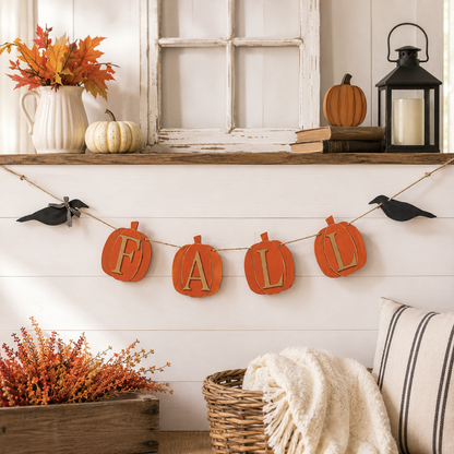 A fall-themed decorative banner spelling 'FALL' hangs from a string in a styled home decor setting with pumpkins, a lantern, a window frame, and autumn foliage.
