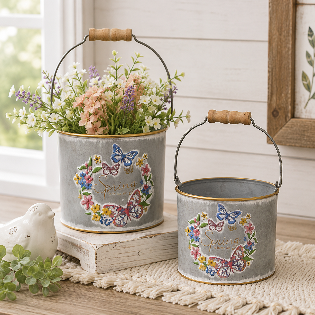 Set of two galvanized spring metal buckets with embossed butterflies and flowers, gold rims, wooden handle grips, and Spring is in the Air lettering.