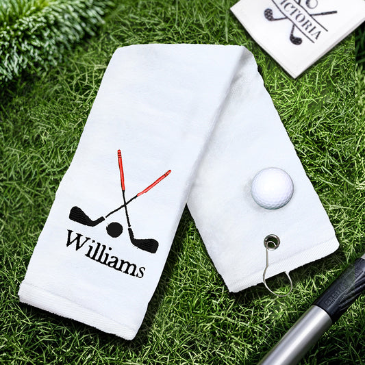 A white golf towel with the customer's personalized embroidered last name, featuring a sturdy clip for easy attachment to golf bags or backpacks.