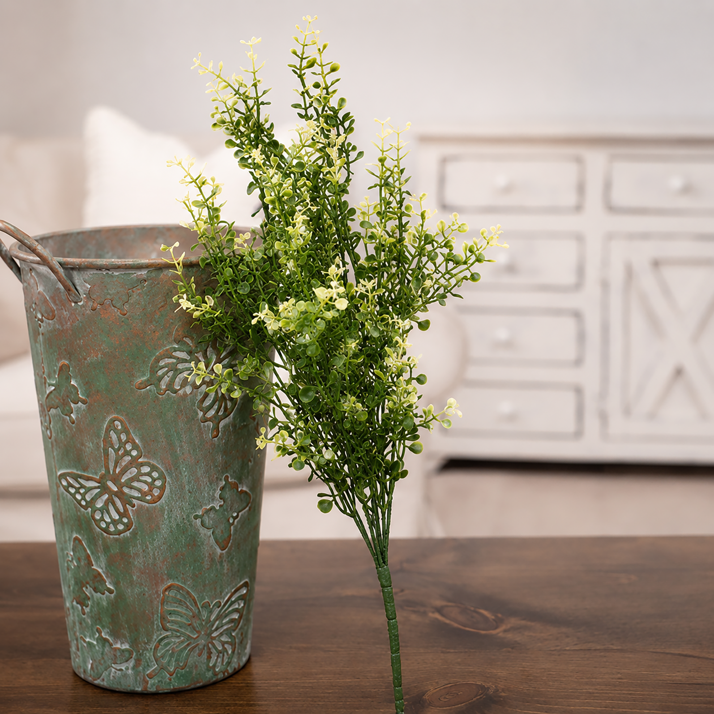 Decorative metal bucket with butterfly designs holding a plant on a wooden surface.