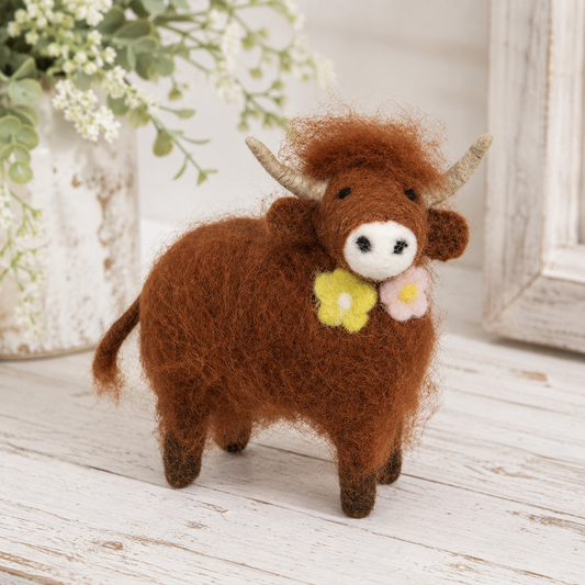 Small felted Highland cow with cream horns, embroidered eyes, and pink and yellow flowers for farmhouse shelf decor