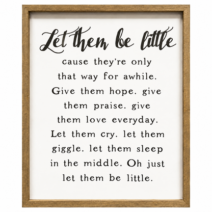 Framed nursery wall art featuring the quote 'Let them be little' in black script and serif text on a white background, enclosed in a light natural wood frame.