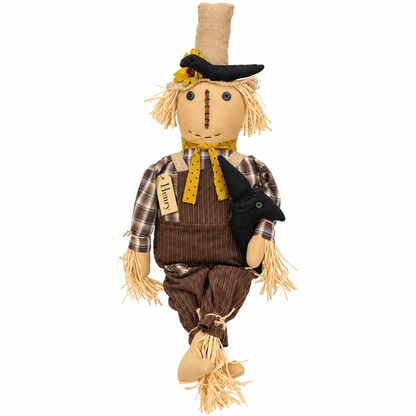 A rustic fabric scarecrow hanging decoration with straw hair, a black hat, brown striped overalls, a plaid shirt, yellow accents, and a small black bird on the side, shown on a plain white background.