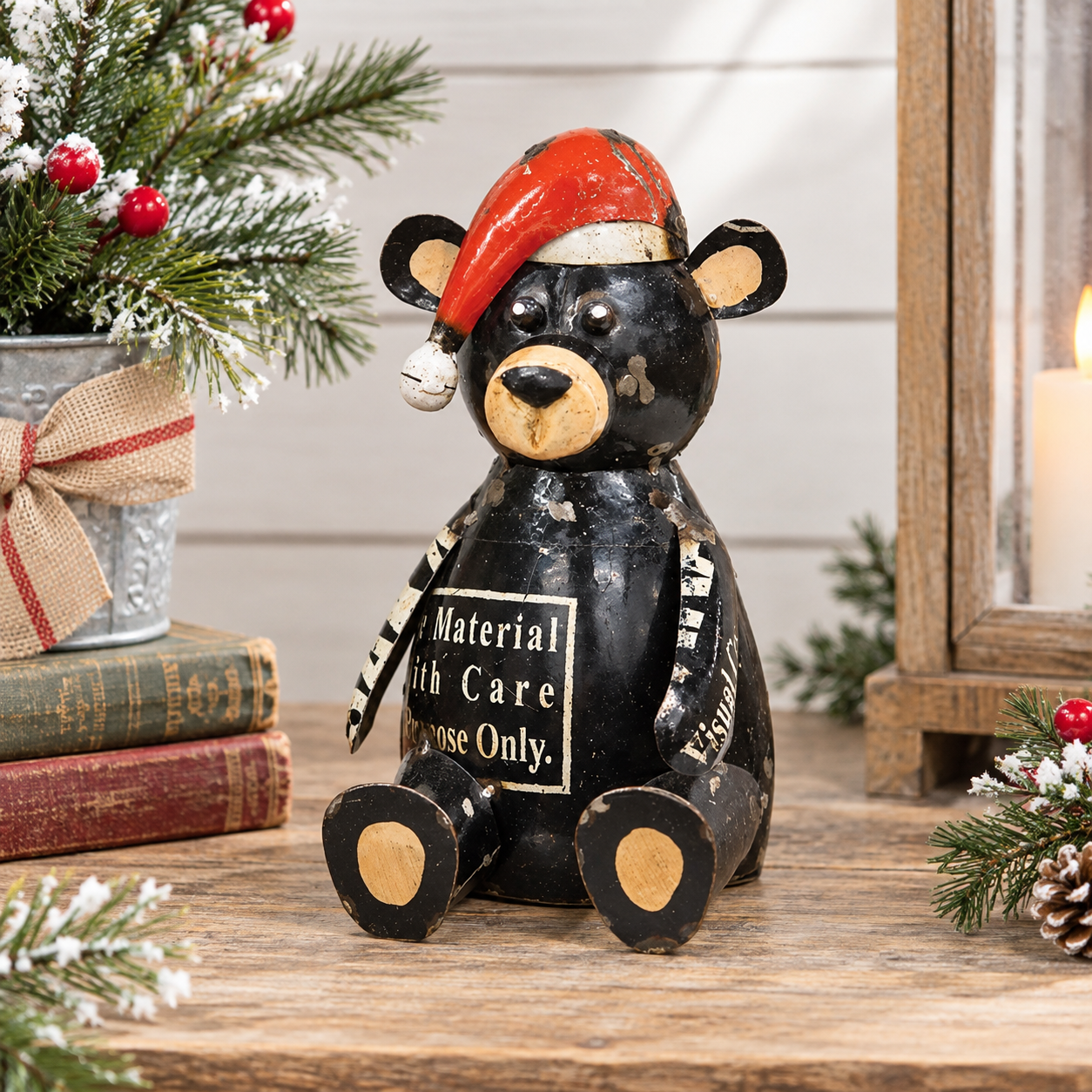 A black bear figurine with a red Santa hat sits on a wooden table, surrounded by holiday decorations including a potted evergreen, books, and a lantern.