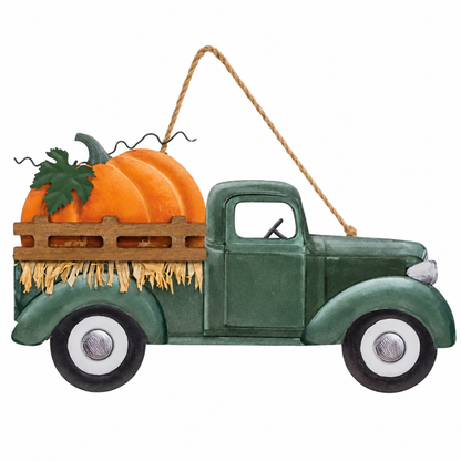A decorative hanging ornament shaped like a vintage green pickup truck carrying an orange pumpkin and hay in the bed, suspended by a rope on a white background.