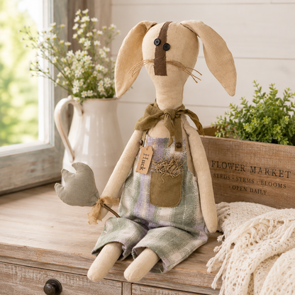 Primitive bunny shelf sitter named Huck wearing blue and green plaid overalls with a moss-filled pocket, brown scarf, and posable ears while holding a plush tulip, displayed as rustic farmhouse spring and Easter home décor.