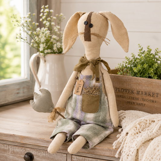 Primitive bunny shelf sitter named Huck wearing blue and green plaid overalls with a moss-filled pocket, brown scarf, and posable ears while holding a plush tulip, displayed as rustic farmhouse spring and Easter home décor.