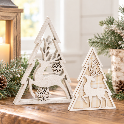 Two decorative wooden Christmas tree ornaments with deer cutouts, displayed on a wooden surface with holiday greenery and a lantern in a softly lit indoor setting.