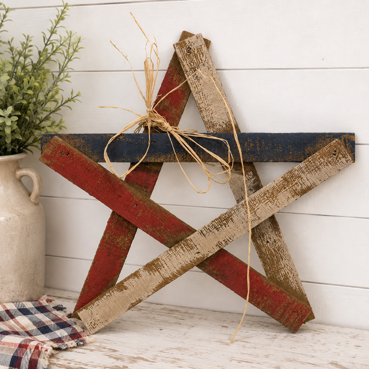 Rustic 16 inch Americana wood lath star with distressed red white and blue finish and decorative straw bow for farmhouse wall decor