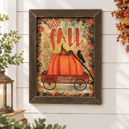 Framed autumn wall art hanging on a white shiplap wall, featuring a large orange pumpkin in a red wagon with the words “Hello FALL” and “The Pumpkin Patch,” surrounded by fall foliage and a crow. Decorative plants and a lantern are visible at the sides.