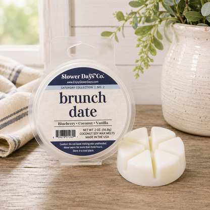 A round package of Slower Days Co. 'brunch date' soy wax melts sits on a wooden surface next to an unpackaged white wax melt piece.