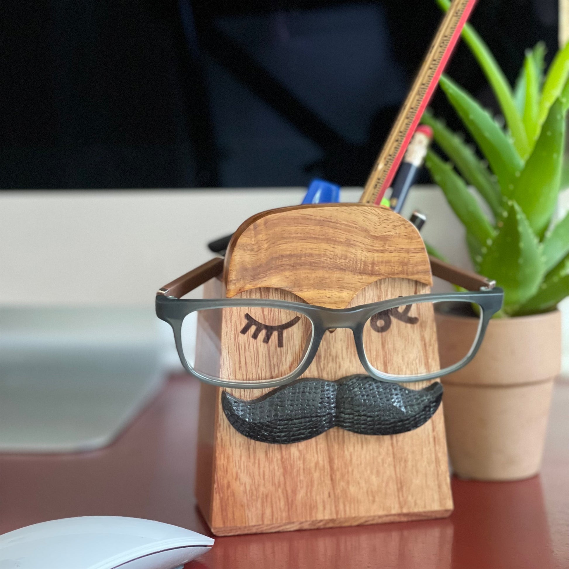 Close-up of wooden eyeglass stand featuring a quirky moustache design, perfect for keeping glasses and a pen in place.