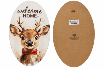 An oval decorative sign shown from both sides: the front features a painted deer with antlers and a red bow tie under the words "welcome HOME," and the back shows a brown backing board with a small hanging hole and printed maker mark.