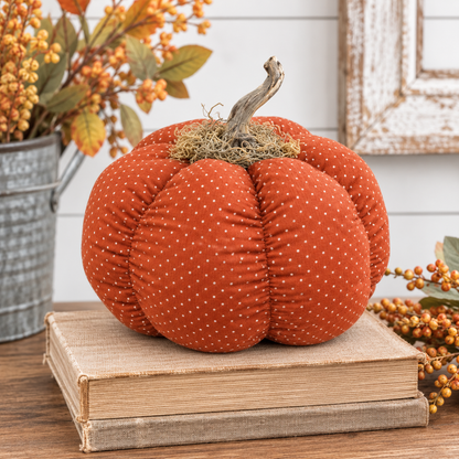 An orange fabric pumpkin decoration with small white polka dots sits on stacked vintage books, styled with autumn berries and a rustic framed picture in the background.