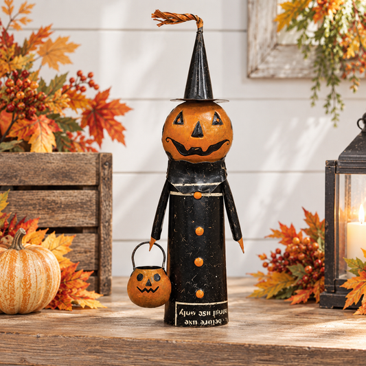 A Halloween decorative figure made from a black tin can with a carved orange pumpkin head, standing on a rustic wooden surface with autumn leaves, a small pumpkin, and a lantern in the background.