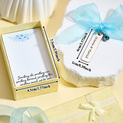 A close-up of the "something blue" charm with a blue ribbon, displaying an overlay with the size of the charm (1.57 inch x 0.39 inch) and the box (2.95 inch x 1.77 inch).