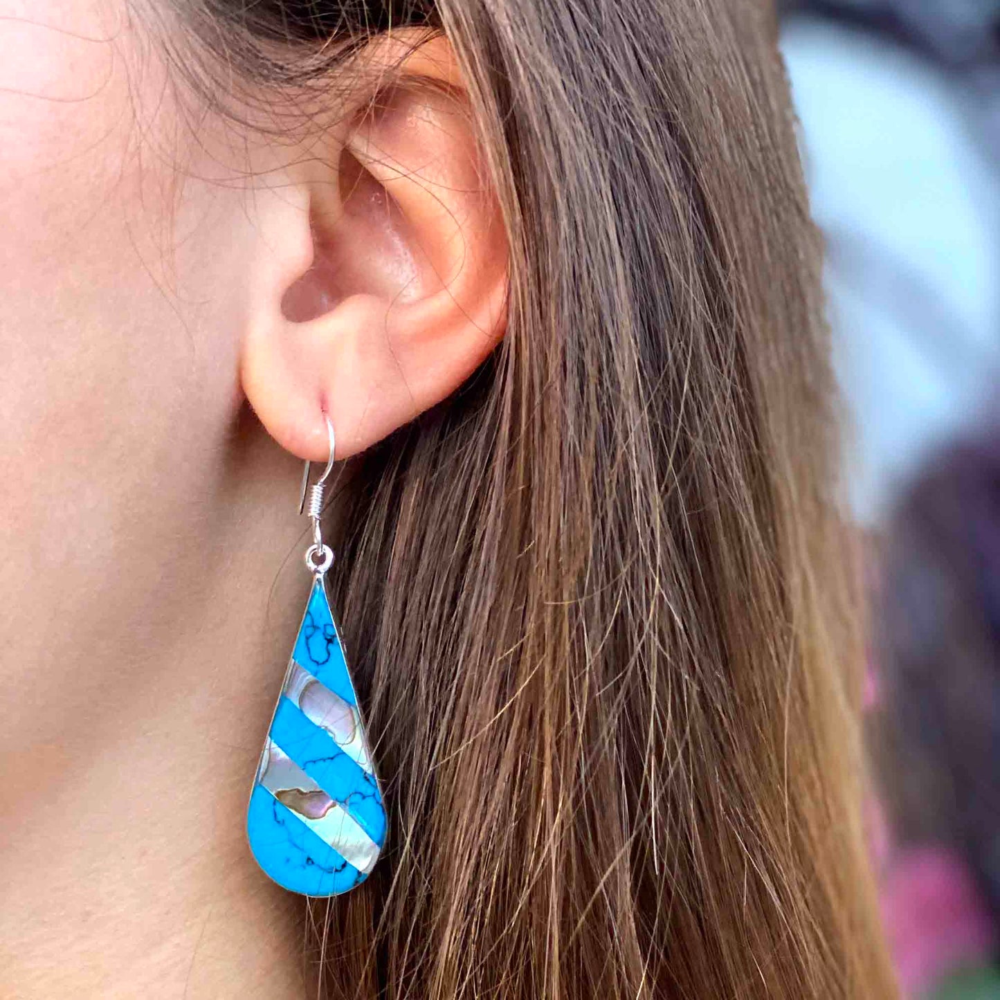 Close-up of iridescent abalone shell and turquoise striped earrings.