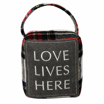 Cube-shaped plaid fabric doorstop with Love Lives Here embroidery and top carrying handle styled with winter farmhouse decor.