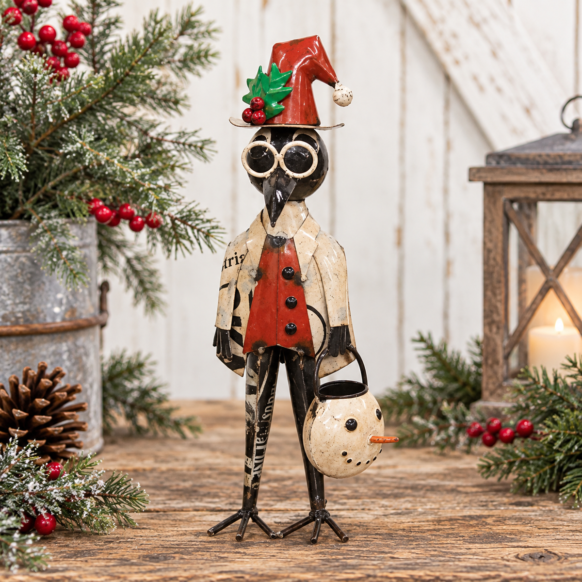 A decorative bird figurine dressed in a holiday coat and Santa hat, holding a snowman bucket, displayed on a rustic wooden surface with Christmas greenery, berries, and a lantern in the background.