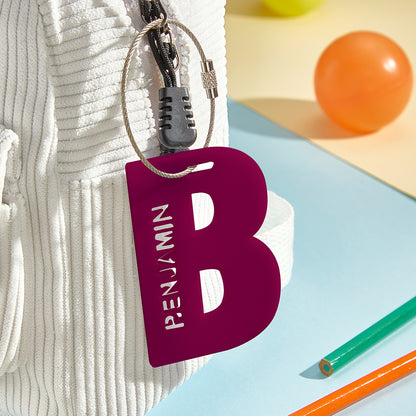 A close-up view of a 3D printed luggage tag shaped like the letter "B" in a maroon-ish red, showcasing its vibrant color and sturdy acrylic material, designed for easy identification.