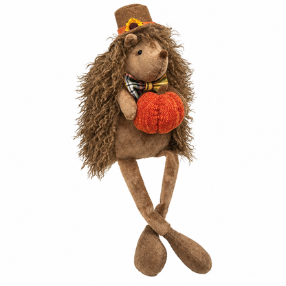 A plush hedgehog doll with curly brown faux-hedgehog hair, wearing a brown top hat with a sunflower and a plaid bow tie, while holding a knitted orange pumpkin against a plain white background.