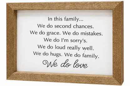 A framed typographic wall sign with a natural wood frame and a white background. The sign features black text reading, 'In this family.