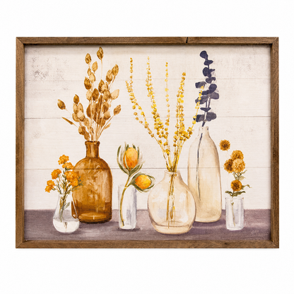 Framed wall art featuring a still life painting of dried and yellow flowers arranged in clear glass vases on a rustic white wood plank background, enclosed in a medium brown wooden frame.