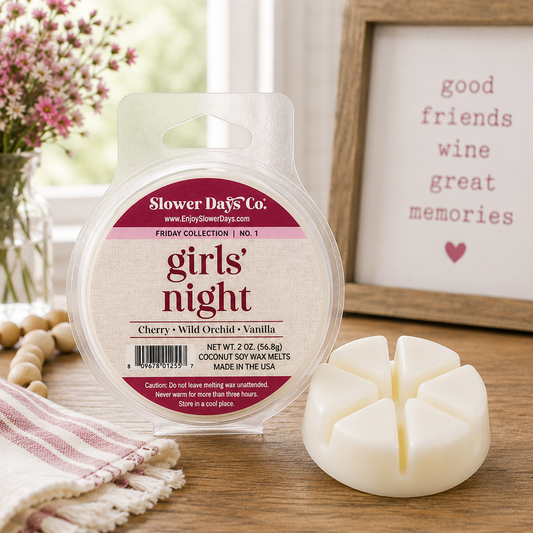 A round plastic package of Slower Days Co. 'girls' night' coconut soy wax melts sits on a wooden surface, with a small white four-wick wax melt holder beside it.