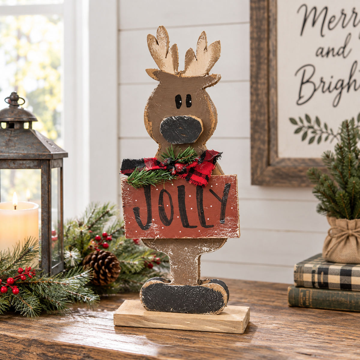 A rustic Christmas decorative sign shaped like a reindeer head holding a wooden sign that says "JOLLY" in black script. The reindeer has light brown antlers and a dark brown face, with a red and black plaid bow and green pine garland around the neck.