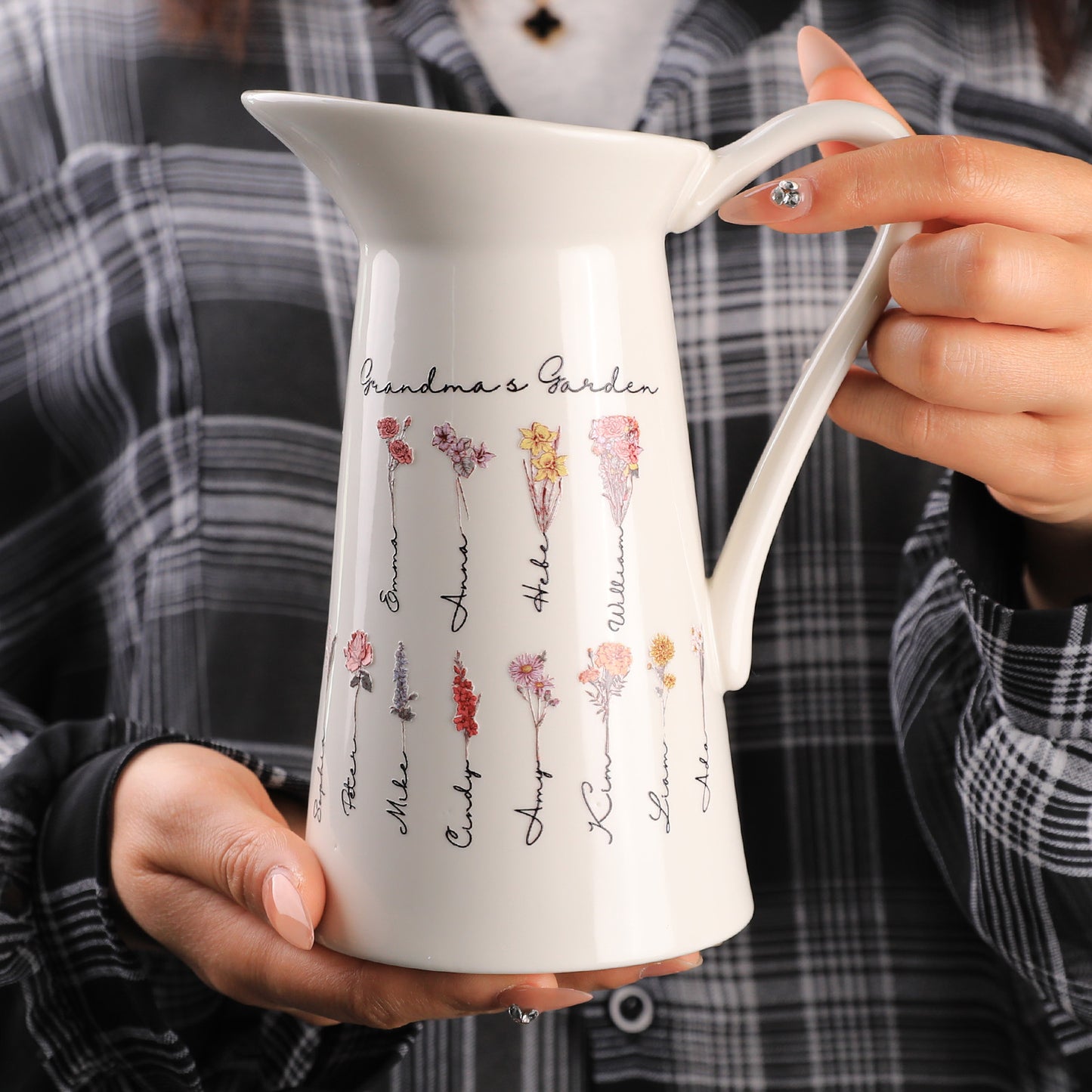 A close-up view of the pitcher-shaped vase being held by someone, highlighting its detailed design with customizable text and birth flowers.