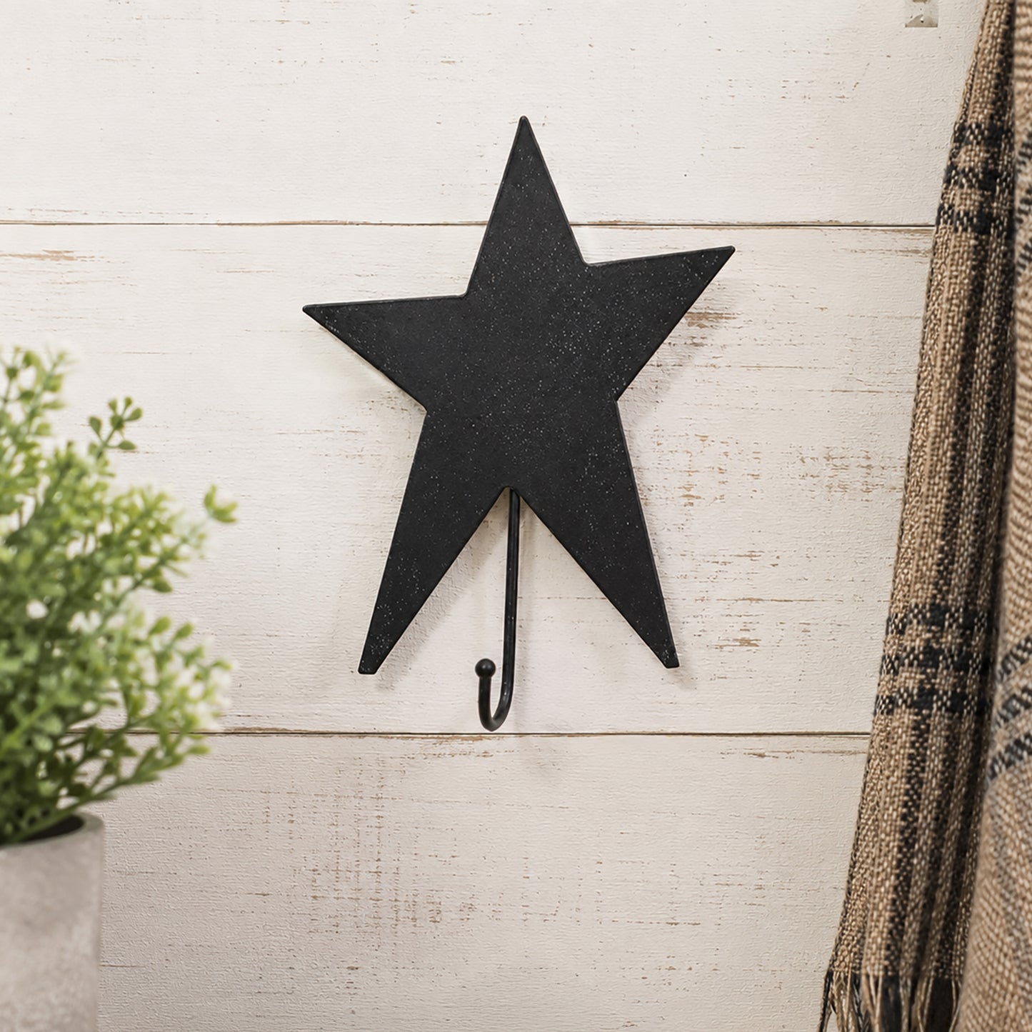 Black star-shaped wall hook on a light wooden background with a plant and blanket.