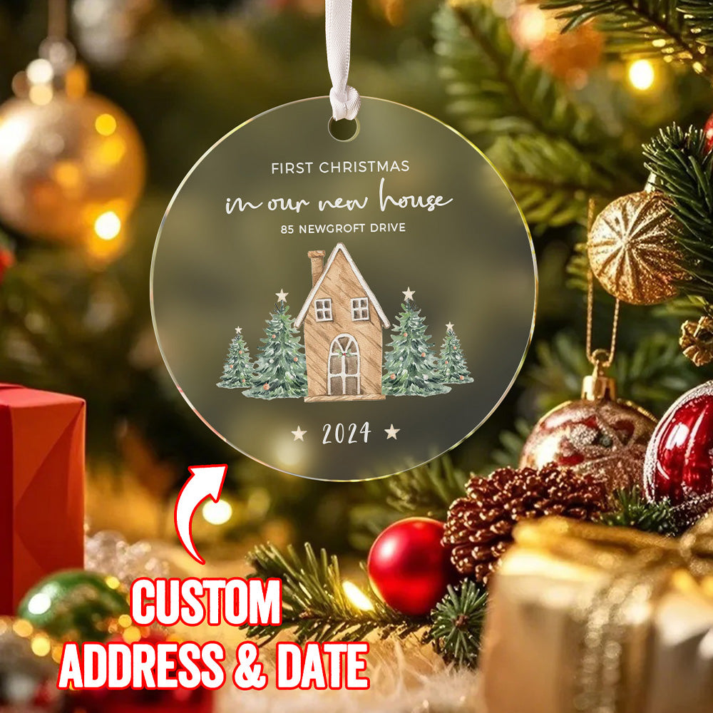 A front view of the personalized Christmas ornament featuring a house surrounded by Christmas trees with the text "First Christmas in our new home." The ornament has a text overlay saying "custom address & date," indicating the personalization options available.