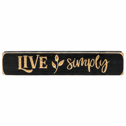 A rectangular black wooden sign with distressed gold lettering that reads 'LIVE simply' and a small leaf motif, shown on a plain white background.