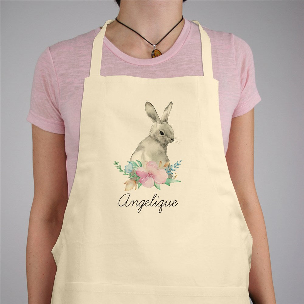 Full-length natural cotton apron featuring a floral Easter bunny design, personalized with a name, adjustable neck strap, and large front pocket, perfect for holiday baking and crafting.