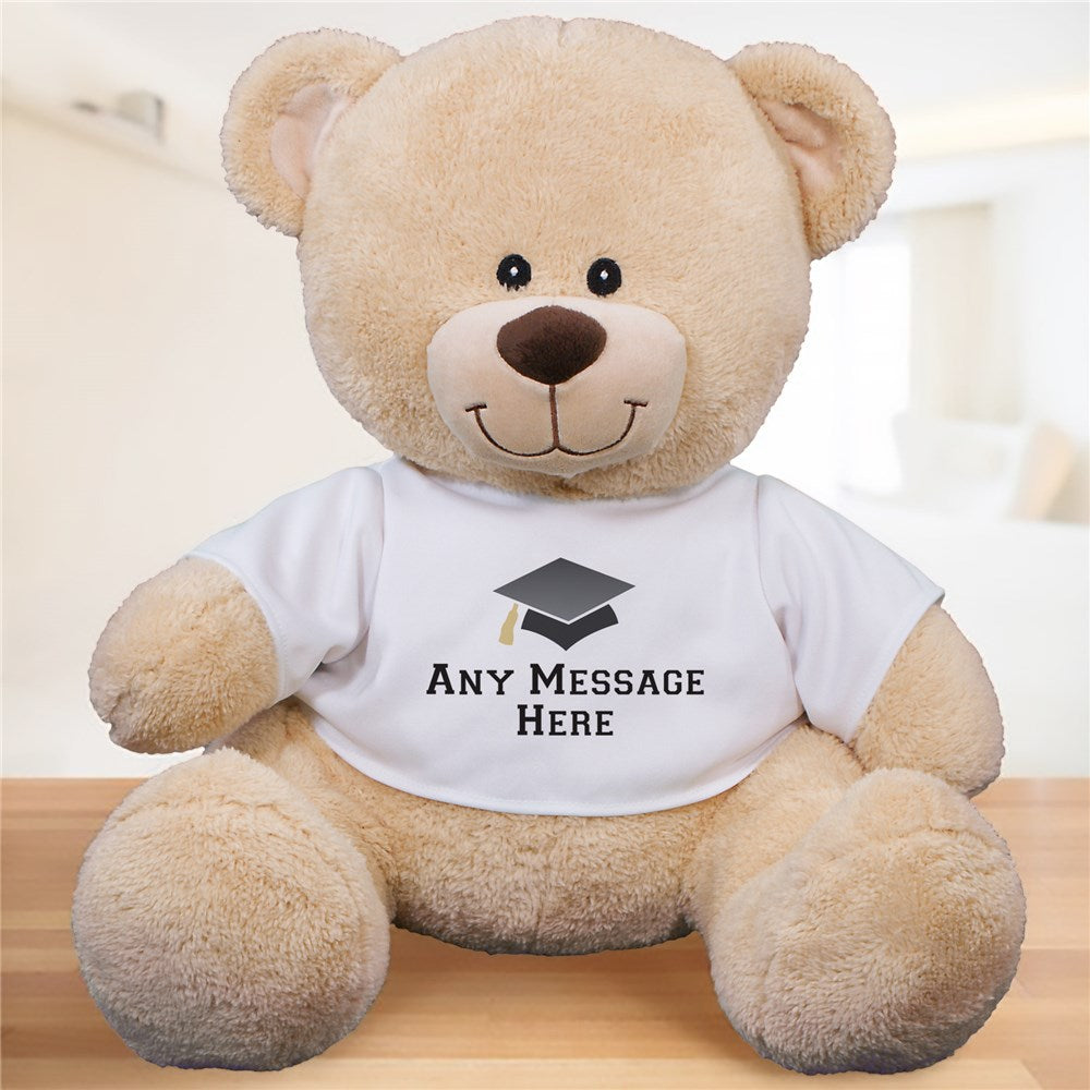A soft, light brown graduation teddy bear wearing a customizable white shirt, available in three sizes.