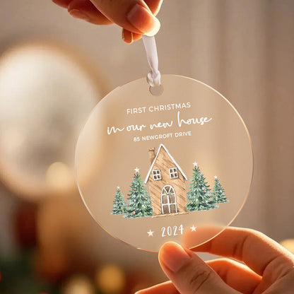 A front view of the personalized Christmas ornament featuring a house surrounded by Christmas trees with the text "First Christmas in our new home," held in hands, ready to be customized with the address and year.