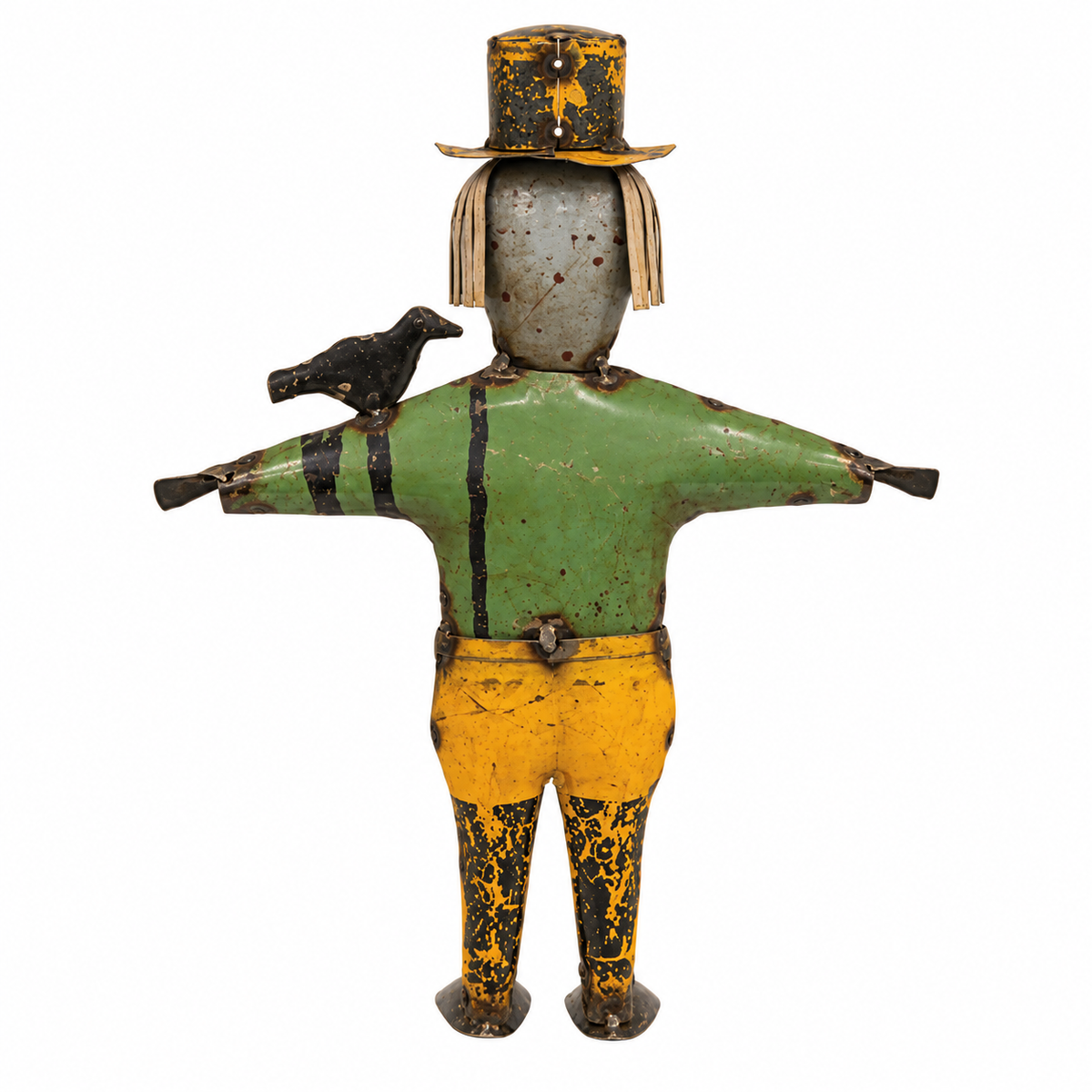 A vintage painted wooden scarecrow figurine with a green shirt, yellow pants, black and yellow mottled hat and boots, and a small black bird perched on its shoulder, isolated on a white background.