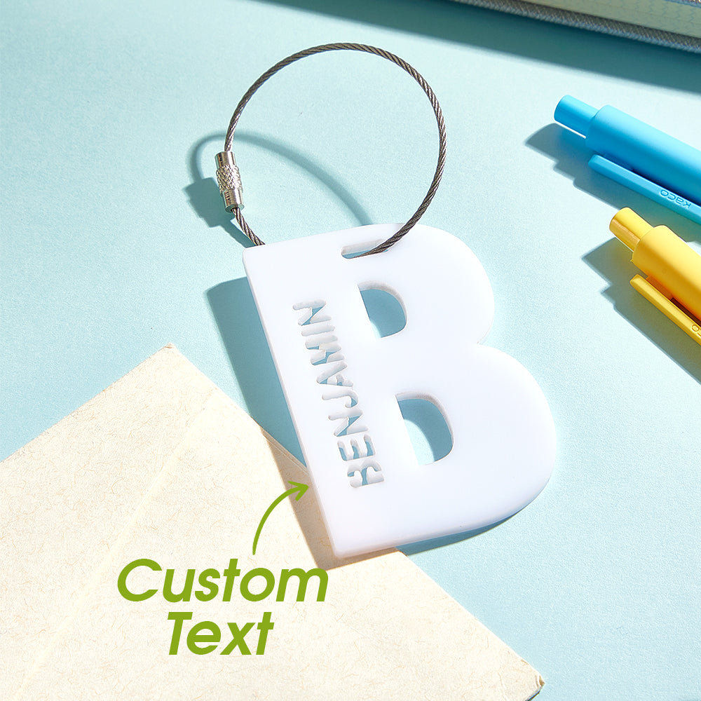 A close-up view of a 3D printed luggage tag shaped like the letter "B" in white, with a text overlay that says "Custom text," highlighting its clean design and personalized touch.