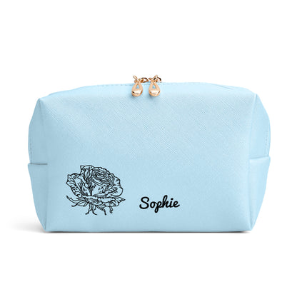 A close-up view of the blue makeup bag, highlighting the delicate personalized design with a birth flower and name.