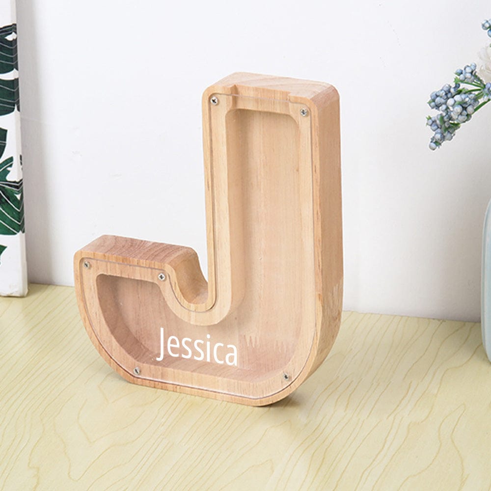 A personalized "J" letter piggy bank, combining light wood with a sleek acrylic surface to track savings.