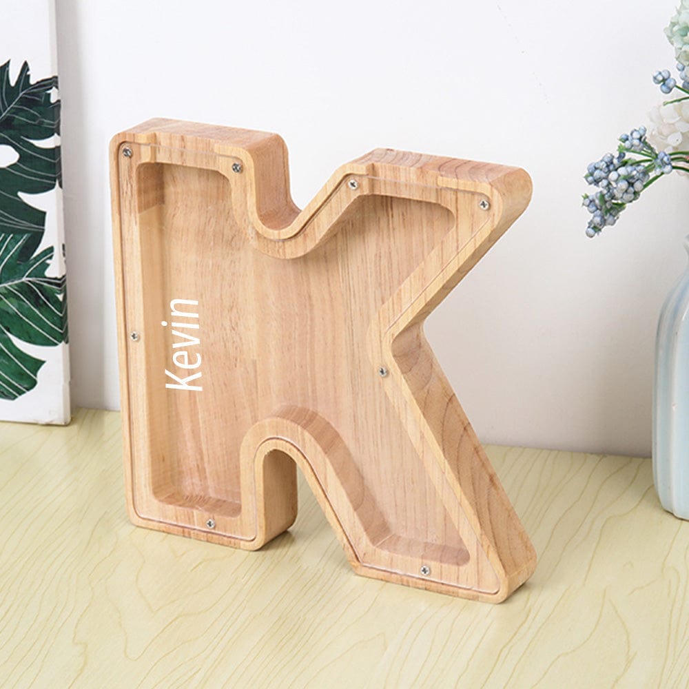 A personalized "K" piggy bank made from light burlywood wood with a transparent acrylic face, perfect for kids to save and track their money.