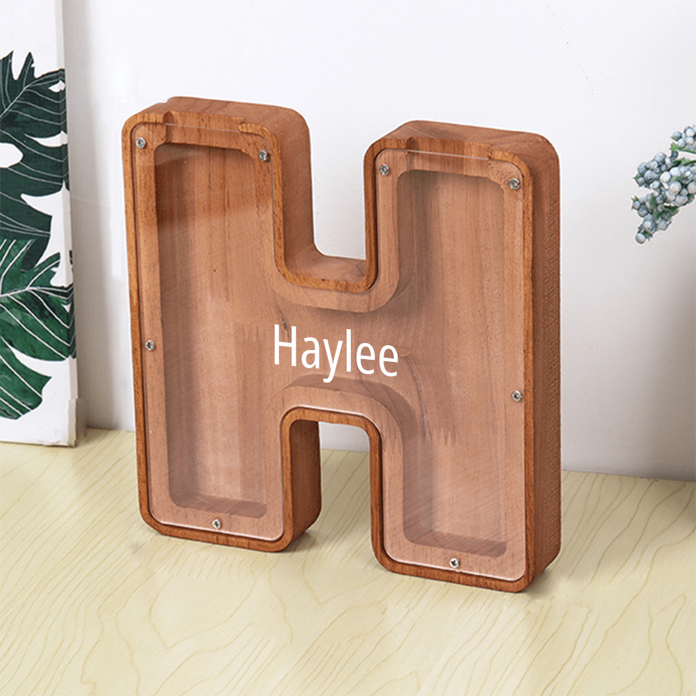 A "H" shaped piggy bank made of brown wood and acrylic, helping kids learn to save in an interactive way.