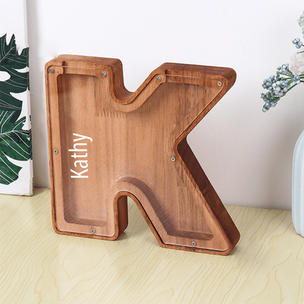 A personalized "K" letter piggy bank in rich brown wood with a clear acrylic panel, perfect for kids to save and track their money.