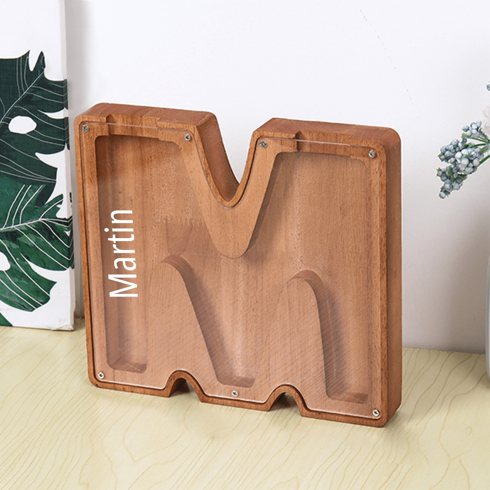 A custom "M" letter piggy bank made of brown wood with an acrylic surface, designed to encourage kids to develop a saving habit.