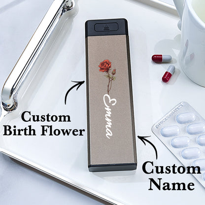 A top view of the weekly pill organizer with text highlighting the customizable name and birth flower design on the cover.