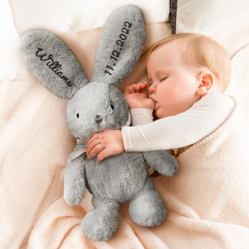 Sleeping baby cuddling a plush bunny – A baby peacefully snuggled up with a gray bunny featuring black embroidered ears.