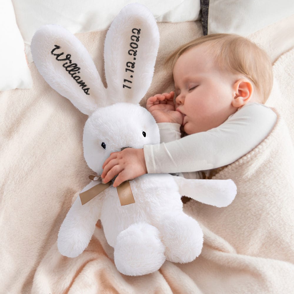 Baby cuddling a plush bunny while sleeping – A baby resting with a white bunny featuring black embroidery.